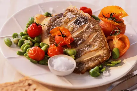 Filet de saint pierre grillé, servi avec des tomates cerises rôties et des fèves, un délice simple et savoureux.
