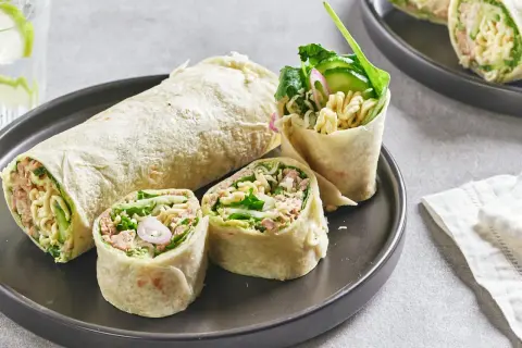 Wrap thon garni de nouilles, concombre et légumes verts, coupé en tronçons sur une assiette.