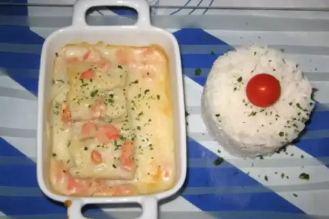 Poisson en sauce normande, parsemé de persil, servi avec une timbale de riz et une tomate cerise.