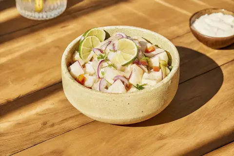 Un bol de ceviche frais, garni de rondelles de citron vert et d'oignon rouge. Une recette légère et savoureuse.