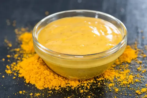 Un bol de sauce pour poisson, d'une belle couleur jaune, est posé sur un lit de poudre d'épices.