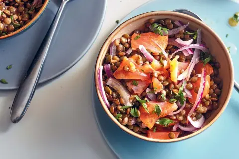 Salade de lentilles aux tomates, oignons rouges et saumon fumé, garnie de persil frais. Un plat coloré et savoureux.