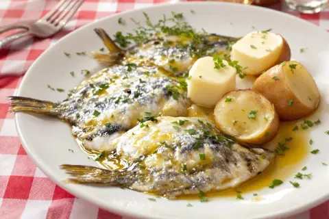 Assiette de harengs marinés avec pommes de terre et persil sur nappe à carreaux rouges.