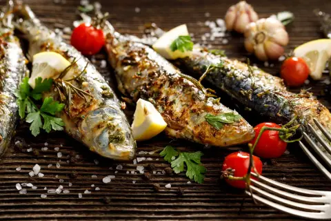 Sardines grillées, citron, tomates cerises, ail et persil sur fond de bois. Faut-il vider les sardines avant de les cuire ? La réponse est dans l'assiette !