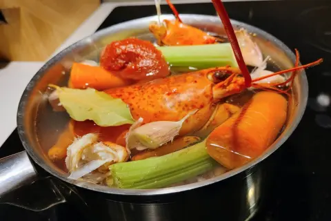 Deux homards entiers mijotent dans un court-bouillon avec carottes, céleri, ail et feuille de laurier.