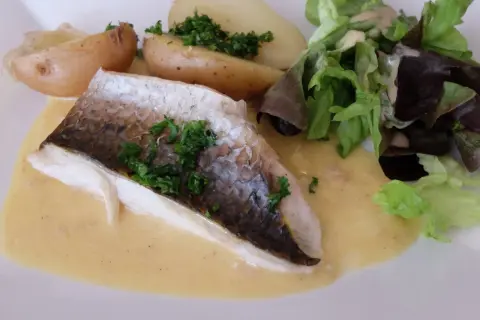 Filet de mulet poisson, servi avec des pommes de terre rôties, une salade verte et une sauce crémeuse.