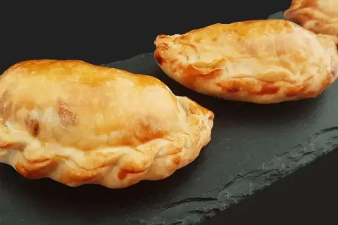 Trois chaussons dorés, un pastel thon savoureux, sur une ardoise sombre.