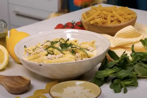 Un plat de pâtes au thon crémeuses, garni de menthe fraîche et de zeste de citron, prêt à être dégusté.