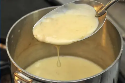 Une cuillère de sauce onctueuse, peut-être un beurre nantais, s'écoule dans une casserole.