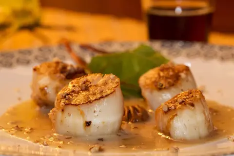 Quatre noix de Saint-Jacques poêlées, dorées et nappées d'une sauce onctueuse, sur une assiette décorée.