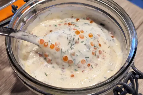Une cuillère de sauce pour saumon crémeuse, parsemée d'aneth et de perles d'œufs de poisson, dans un bocal en verre.