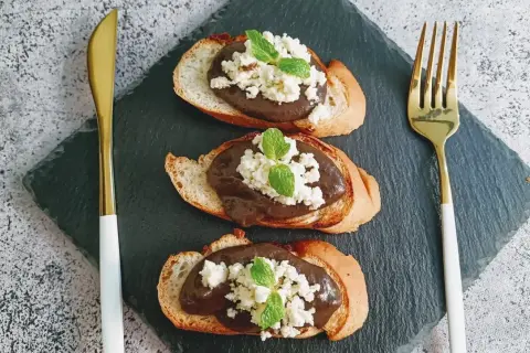 Trois toasts de pain grillé garnis d'une pâte foncée, de fromage blanc émietté et de feuilles de menthe. Une présentation élégante pour une tapenade de la mer revisitée.