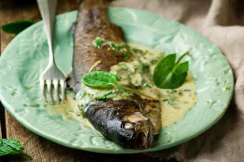 Poisson entier nappé d'une onctueuse sauce à l'oseille, garni de feuilles vertes fraîches, sur une assiette menthe.