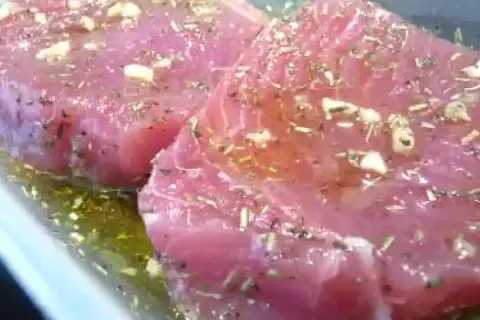 Deux beaux steaks de thon poisson marinés avec de l'ail et des herbes dans une huile dorée.
