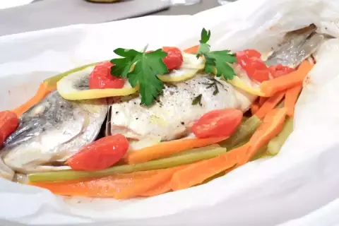 Dorade au four en papillote, garnie de tomates cerises, rondelles de citron, carottes et persil. Un plat sain et savoureux.