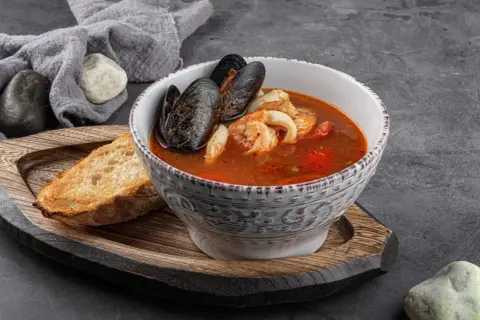 Bol de soupe de poisson aux moules et crevettes, servi avec une tranche de pain grillé et une touche de sauce rouille.