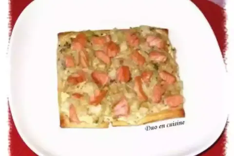 Tarte rectangulaire garnie de poireaux et de morceaux de saumon fumé, servie sur une assiette blanche.
