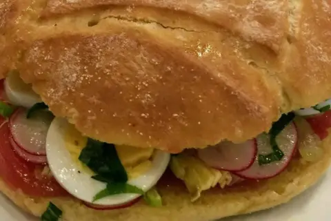 Un délicieux pan bagnat garni de tomates, œufs durs, radis et herbes fraîches. Parfait pour une recette facile et savoureuse.