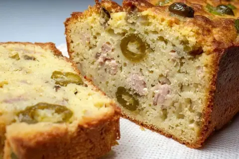 Tranche d'un cake au thon moelleux, garni d'olives vertes et de morceaux de thon. Parfait pour un apéritif ou un repas léger.