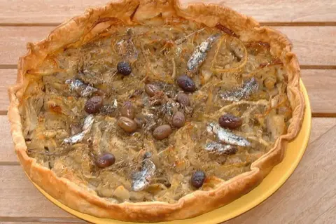 Pissaladière garnie d'anchois et d'olives, sur une pâte brisée ou feuilletée dorée.