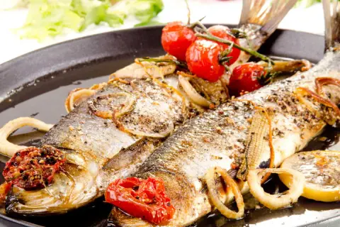 Deux poissons entiers, le hareng, rôtis avec des tomates cerises, des oignons et des rondelles de citron sur un plat noir.