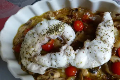 Un délicieux filet de congre au four, parsemé d'herbes, servi avec des tomates cerises et des champignons dans un plat blanc ondulé.