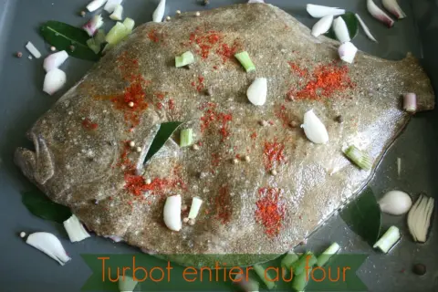 Un turbot entier est préparé pour être rôti au four, assaisonné de paprika, d'ail, d'oignons et de grains de poivre.