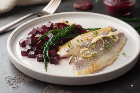 Deux filets de limande cardine poêlés, servis avec des dés de betterave et de la salicorne, garni de zestes de citron et de pousses vertes.