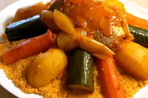Un plat généreux de couscous garni de poisson, carottes, courgettes et pommes de terre, le tout nappé d'une sauce savoureuse.