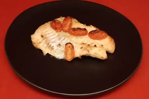 Un filet de dorade sebaste cuit, garni de tomates cerises rôties, servi sur une assiette noire.