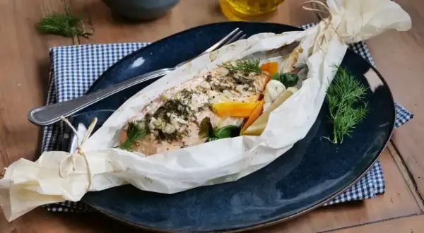 Poisson au four, savoureux et parfumé, enveloppé dans du papier sulfurisé avec des légumes et des herbes fraîches.