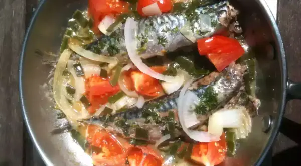 Deux maquereaux mijotent dans une poêle avec des tomates, des oignons et des herbes. Le temps de cuisson maquereau à la poêle est presque terminé.