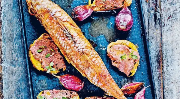 Un rouget barbet rôti sur un plateau avec des toasts tartinés de rillettes, des oignons rouges et des herbes.