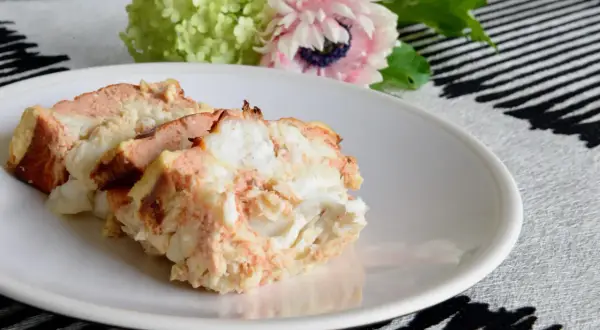 Tranches de terrine de lotte savoureuse sur une assiette blanche, avec des fleurs en arrière-plan.
