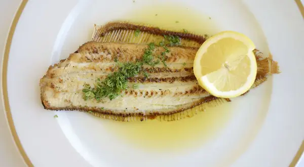 Un plat de sole meunière, un poisson délicatement poêlé, nappé d'une sauce au beurre et citron, garni de persil frais et d'une tranche de citron.