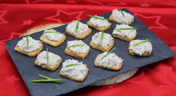Douze toasts garnis de rillettes de maquereau, décorés d'une fine herbe verte, présentés sur une ardoise.