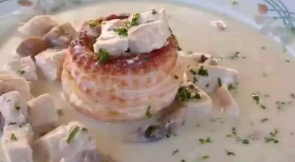 Un délicieux vol au vent aux crevettes, garni de morceaux de volaille et de persil frais, baignant dans une sauce crémeuse.