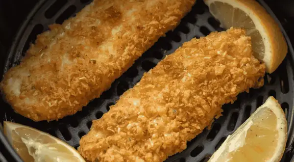 Deux filets de poisson pané dorés et croustillants, accompagnés de quartiers de citron, prêts à être dégustés dans une friteuse à air.