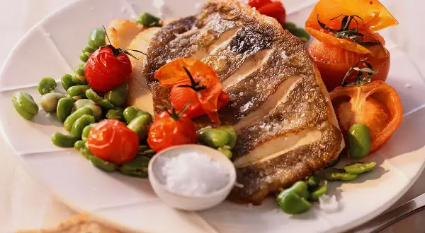 Filet de saint pierre grillé, servi avec des tomates cerises rôties et des fèves, un délice simple et savoureux.