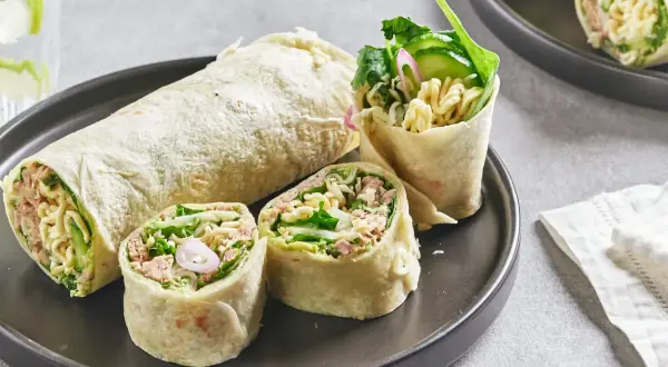 Wrap thon garni de nouilles, concombre et légumes verts, coupé en tronçons sur une assiette.