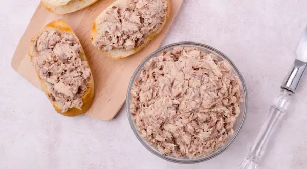 Tranches de pain garnies de rillettes de poisson, un bol rempli de rillettes de poisson et un couteau.