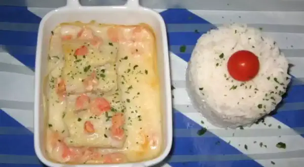 Poisson en sauce normande, parsemé de persil, servi avec une timbale de riz et une tomate cerise.