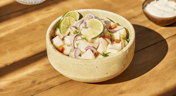 Un bol de ceviche frais, garni de rondelles de citron vert et d'oignon rouge. Une recette légère et savoureuse.