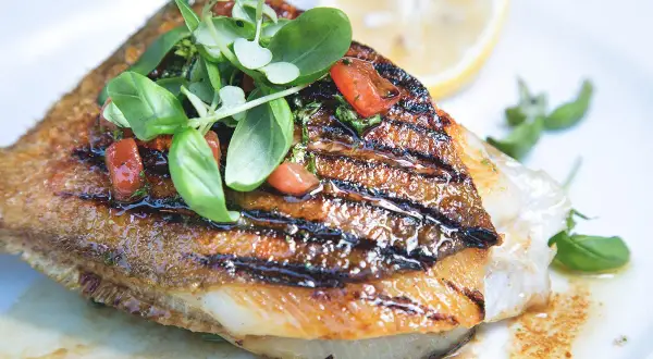 Un délicieux saint pierre poisson grillé, garni de tomates et de basilic frais, servi avec un quartier de citron.