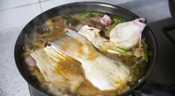 Morceaux de poisson mijotent dans une sauce matelote fumante avec des oignons et des herbes.