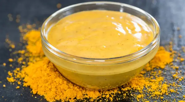 Un bol de sauce pour poisson, d'une belle couleur jaune, est posé sur un lit de poudre d'épices.
