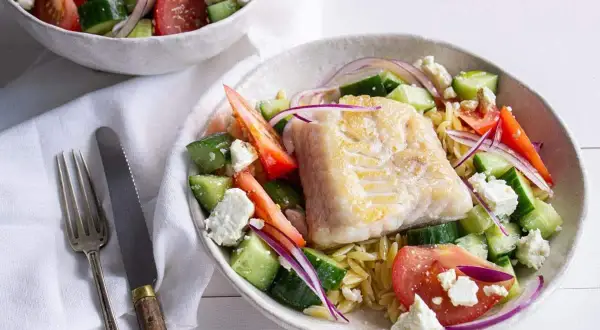 Salade de poisson méditerranéenne avec poisson blanc poêlé, concombre, tomate, oignon rouge et feta sur un lit de pâtes orzo.