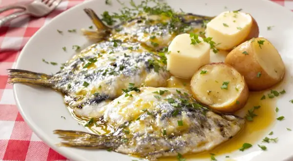 Assiette de harengs marinés avec pommes de terre et persil sur nappe à carreaux rouges.
