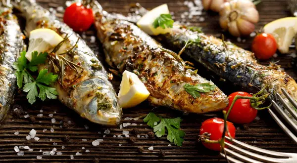 Sardines grillées, citron, tomates cerises, ail et persil sur fond de bois. Faut-il vider les sardines avant de les cuire ? La réponse est dans l'assiette !
