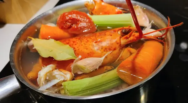 Deux homards entiers mijotent dans un court-bouillon avec carottes, céleri, ail et feuille de laurier.